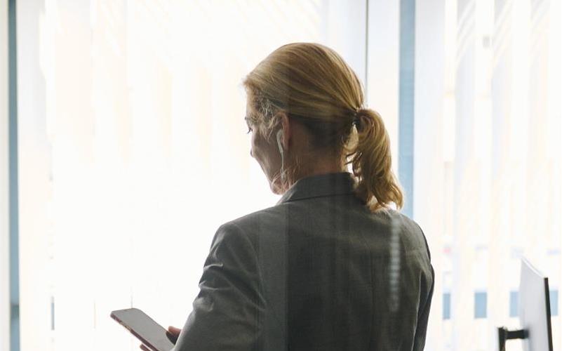 Eine Frau steht in einem Bürozimmer und hält ein Smartphone in der Hand (gestellte Szene). Foto: Annette Riedl/dpa